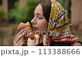 Slow motion. Close-up. A woman in a headscarf eating a freshly baked croissant while sitting at a table a city cafe outdoors on a summer day. The woman enjoys the taste and closes her eyes smiling. 113388666