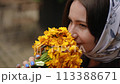 Slow motion. Close-up. Cute brunette woman in a headscarf smell a yellow flower bouquet and smiling while sitting outdoors on a summer day. 113388671