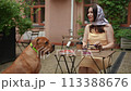 Slow motion. Beautiful woman smiling while sitting at a table on a summer day outside. A large dog sits next to the table and looks at the camera. 113388676