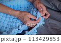 A woman makes a blue blanket for her grandson with her own hands. 113429853
