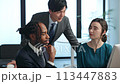 オフィスでパソコンを見ながら会話する多国籍ビジネスパーソンのグループ 113447883