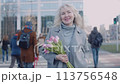 A smiling senior woman with flowers in crowd 113756548