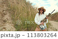 Beautiful young woman holding a shotgun on a field 113803264