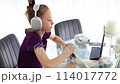 A young girl wearing headphones is sitting at a table using a laptop computer 114017772