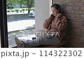 Cafe windowsill woman takes off headphones and starts typing on laptop keyboard. Cafe cozy atmosphere woman working in cafe typing at laptop keyboard Woman embraces working in cafe productivity. 114322302