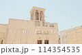 House in traditional Arabic architecture with wind tower. Traditional Arabic style building with windcatcher tower and palm leaves thatched roof. Old Dubai, UAE. Sounds call to prayer in Arabian city 114354535