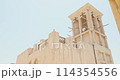 House in traditional Arabic architecture with wind tower. Traditional Arabic style building with windcatcher tower and palm leaves thatched roof. Old Dubai, UAE. View of rooftops of old Arab city 114354556