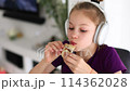 Girl with headphones munching on a sandwich, satisfying her food craving 114362028