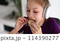 A young girl in headphones enjoys her ice cream cone with her hand and mouth 114390277