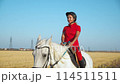 A woman in a red uniform walks on a white horse in a field of hay Moves towards the camera Side view Middle distance medium shot 114511511