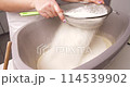 A confectioner sifts flour to knead the dough for baking a confectionery product. 114539902