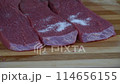 Hands with black rubber gloves gently applying salt on the raw beef slices 114656155