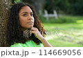Beautiful mixed race African American girl biracial teenager young woman outside sad or depressed sitting leaning against a tree 114669056