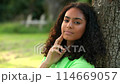 Beautiful mixed race African American girl biracial teenager young woman outside sad or depressed sitting leaning against a tree 114669057