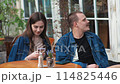 A young couple. Denim clothes. On a date in a vintage restaurant, outside. They are talking. Fooling around 114825446