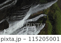 A waterfall with a green forest in the background. The water is clear and calm. The waterfall is surrounded by rocks and trees 115205001