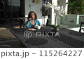 Asian woman is sitting on black ironed table and drinking tea on a terrace, enjoy morning fresh air with view. 115264227