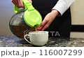 Close-up female hands pour tea from a glass teapot into a white mug on a black marble table. International Tea Day. 116007299