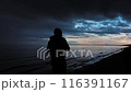 Contemplative persons silhouette by the calm shore at twilight, under a dramatic evening sky 116391167