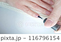 Gel polish manicure step-by-step guide. Step 7 Nails base coat. A woman applies a transparent gel base coat to the little finger of her right hand. At-home manicure 116796154