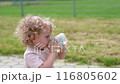 A little curly girl walks down the street and drinks water from a baby bottle. 116805602