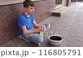 A beggar boy with alcohol in his hands asks for alms on the street. 116805791