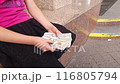A girl on the street near a bank is counting large dollar bills. 116805794