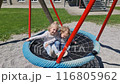 Little children ride on a swing. Two girls ride each other and play on the playground. 116805962