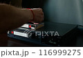 A man lays out VHS tapes on a VCR. 116999275