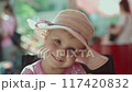 Happy girl in rays of sun. Funny little girl smiling and looking at camera. Concept of a happy childhood. Child shakes her head to music or is in a great mood, adjusts hat and takes it off at end. 117420832