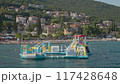 Experience a floating water park near a coastal town with scenic hill backdrop for aquatic fun 117428648