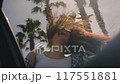 Woman enjoys the palm trees of seaside road. A girl leans out of window of car. Hair in the wind 117551881