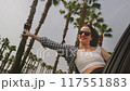Woman leans out of car window gracefully waving hand in rhythm of favorite music against palm trees 117551883