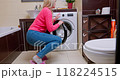 Happy woman checking spotless laundry after successful wash in cozy bathroom, wearing pink sweater and blue jeans 118224515