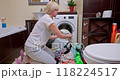 Woman sorting laundry on the bathroom floor, separating whites and colors for washing in a cozy, well-lit bathroom 118224517