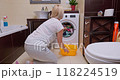 Woman unloading freshly washed clothes from washing machine in a small, bright bathroom 118224519