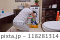 Woman unloading laundry into a plastic basin in a small, bright bathroom 118281314