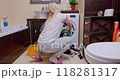 Woman in her 30s finishing laundry, placing last clothes into washing machine in a bright bathroom 118281317