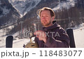Relaxed male skier holds helmet taking off ski goggles standing on lively trail against mountains 118483077
