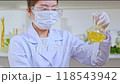 Scientist is stirring yellow solution in volumetric flask to observe experiment. Laboratory background with experimental tools and herbals in the background, suitable as a sample experimental video. 118543942
