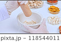 Close-up of a scientist pounding poria cocos wolf in a mortar and pestle with a wooden pestle. Placed on a white table with glass containers containing herbs inside. 118544011