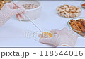 A scientist is stirring a clear petri dish containing a thick, dark yellow gel with a small glass spoon. Around the table are herbs, glassware, and white mortar. 118544016