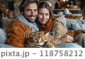 A couple holding their cat, wrapped in blankets, enjoying a cozy evening at home 118758212
