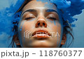 A serene moment of calm as vibrant blue smoke flows around a woman's face in an artistic display of color and emotion 118760377