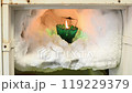 The freezer compartment of the refrigerator is covered with pieces of ice in which there is a burning candle 119229379