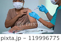 A man is getting a shot and a nurse is administering it. The man is wearing a mask and the nurse is wearing gloves 119996775