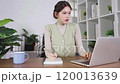 A woman is writing in a notebook while sitting at a desk with a laptop 120013639