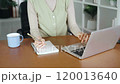 A woman is writing in a notebook while sitting at a desk with a laptop 120013640
