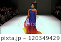 Model showcases a vibrant one shoulder dress with a colorful gradient while confidently walking the runway at a fashion show, embodying elegance and style in motion 120349429