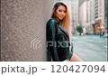 Young woman leans against a wall in a city street, showcasing a variety of stylish outfits while posing confidently for the camera during a fashionable photoshoot 120427094